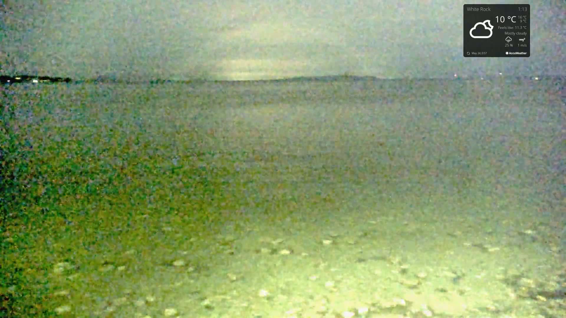 A mostly cloudy, 10°C day is shown over a calm body of water, with a distant shoreline visible under a gray sky.