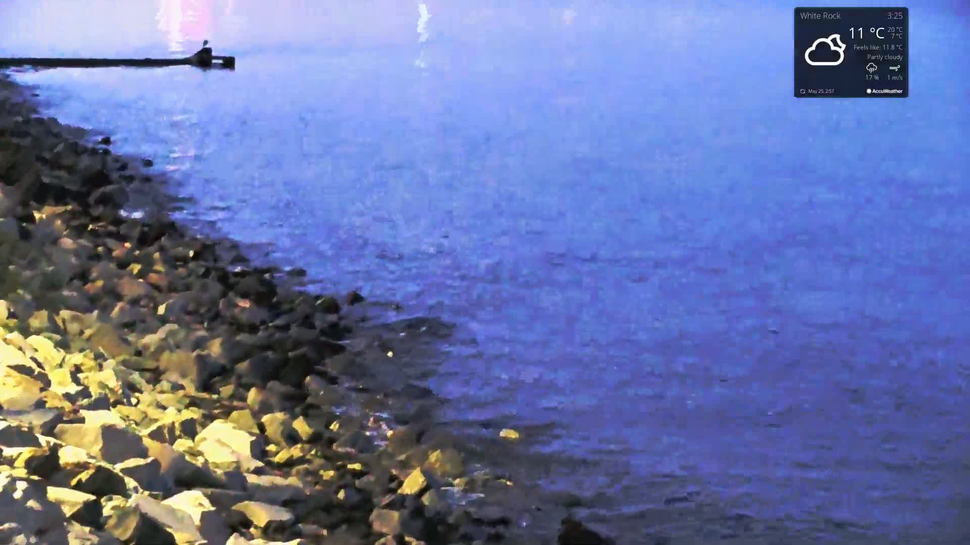 A rocky shoreline meets calm, blue water under partly cloudy skies.