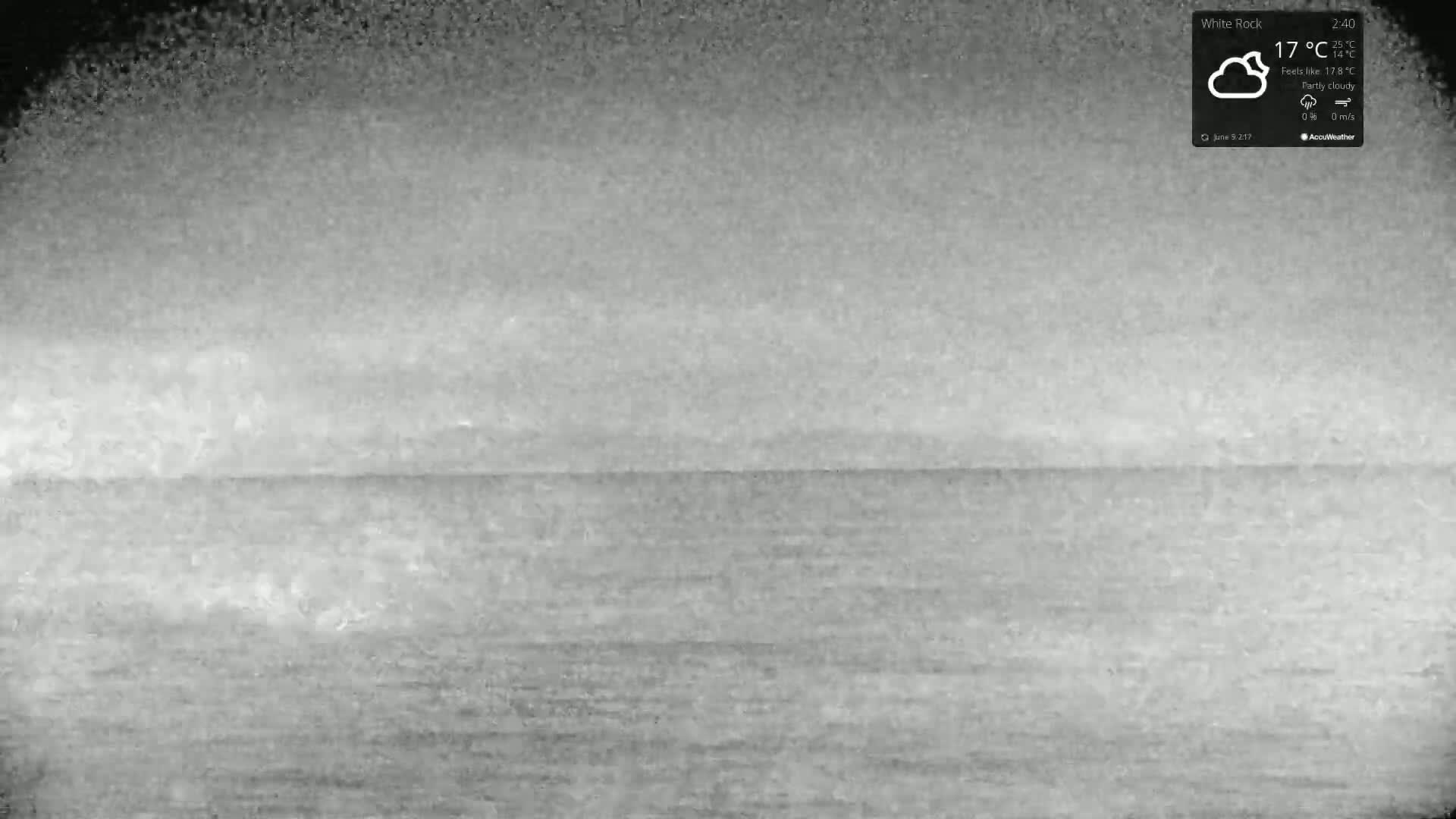 A grayscale image shows a mostly calm body of water under a partly cloudy sky.