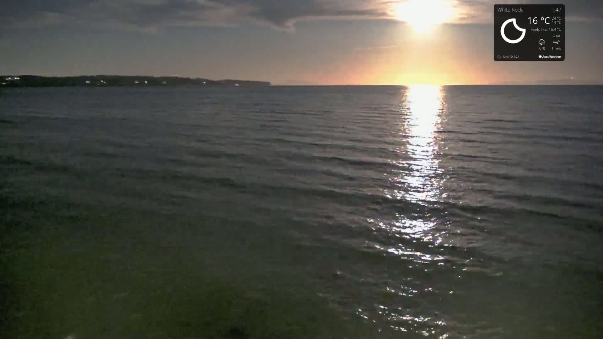 A calm body of water reflects the setting sun under a clear sky.