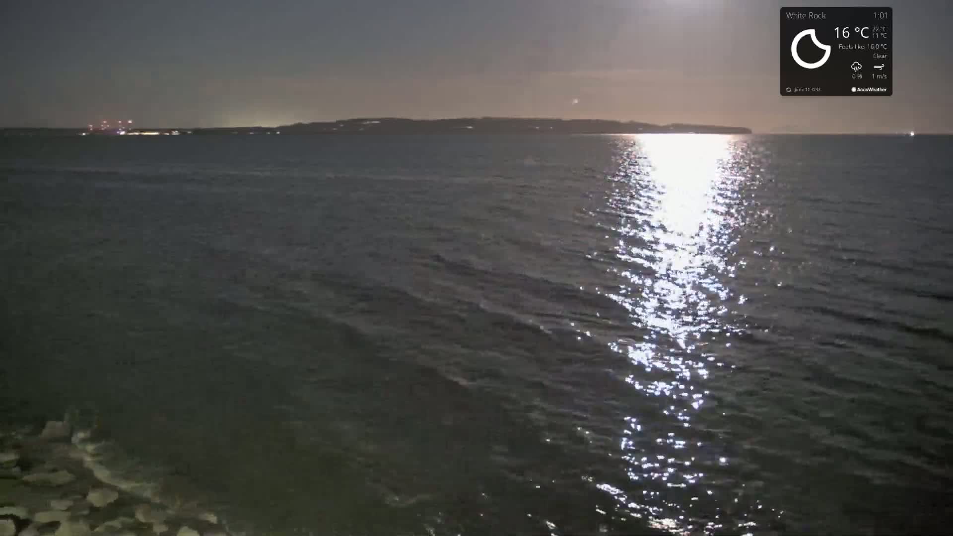 A calm, dark body of water reflects the light of a setting sun under a clear night sky.