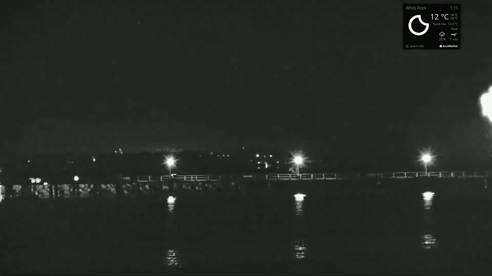A nighttime, clear view of a pier extending over dark water, illuminated by several lights.