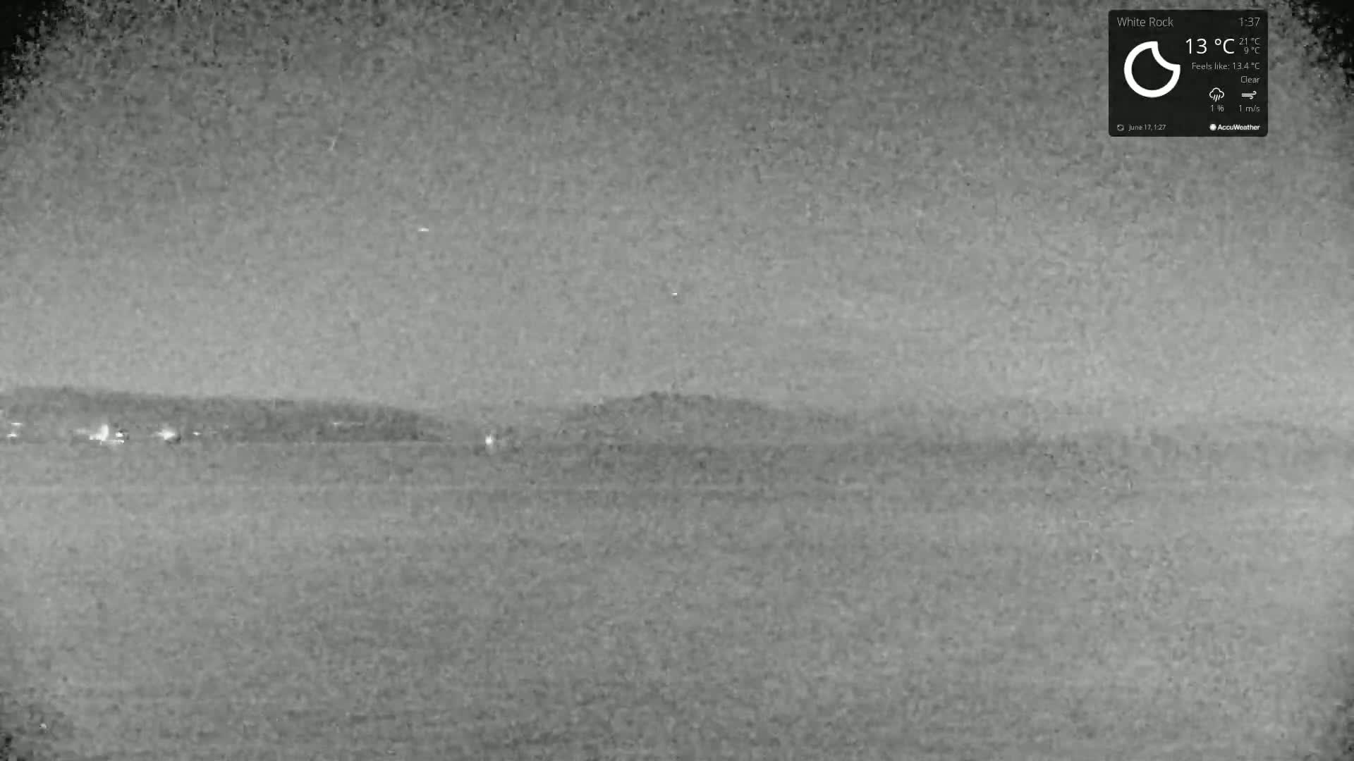 A nighttime, clear-weather view shows a dark body of water in the foreground with faintly lit land in the distance.