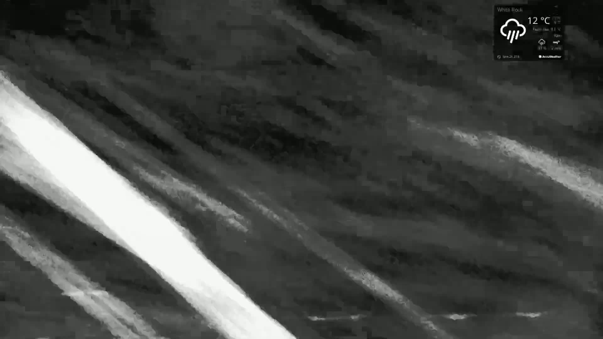 A grayscale image depicts a stormy sky with dark, streaked clouds and a bright diagonal streak of light.