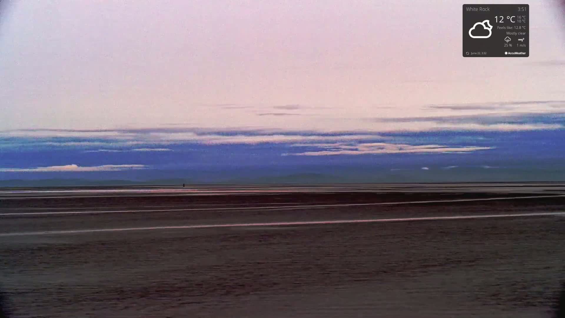 A mostly clear, cool sky over a dark, flat expanse of land near a body of water.