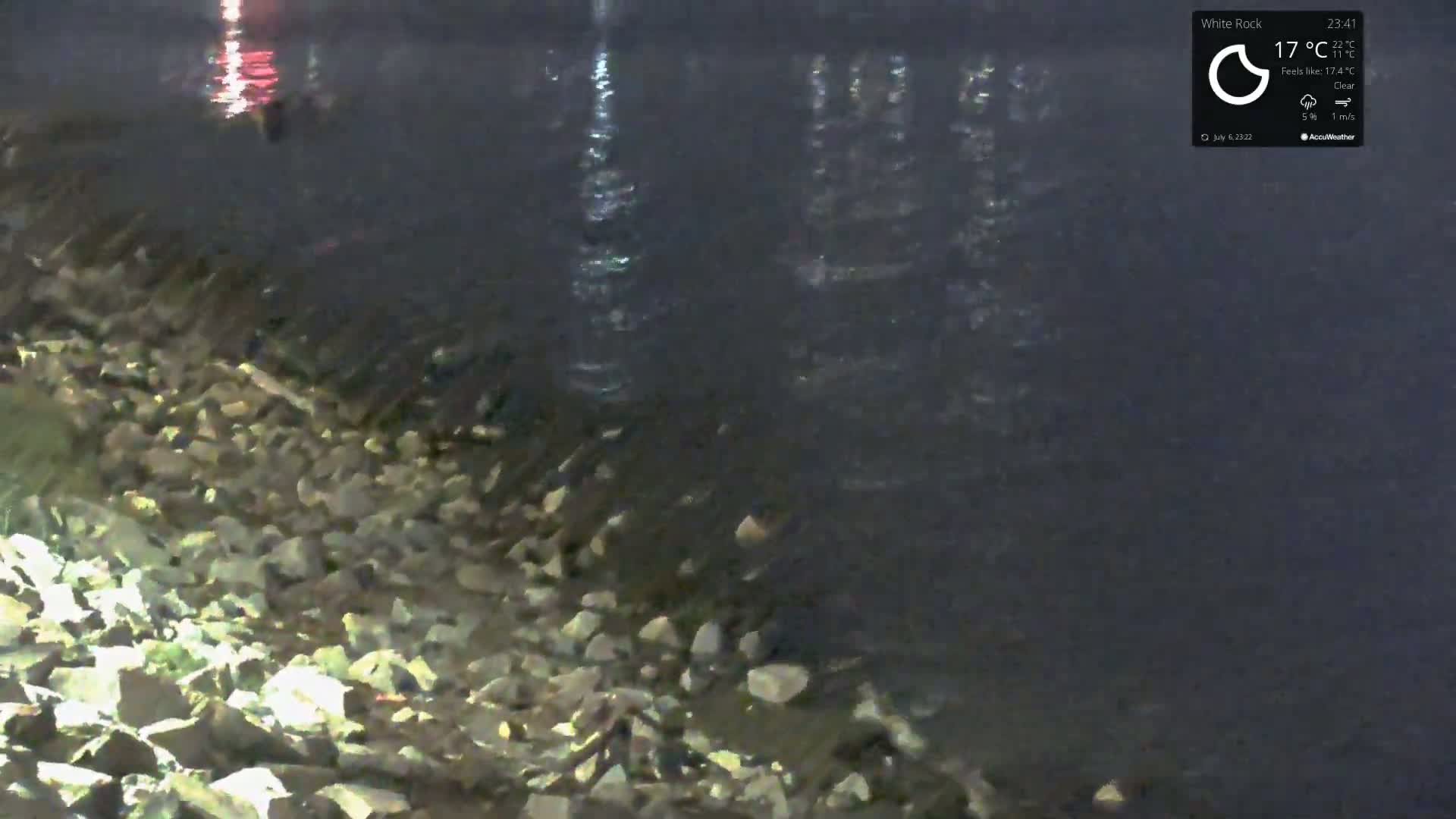 A rocky shoreline meets dark water under a clear night sky.