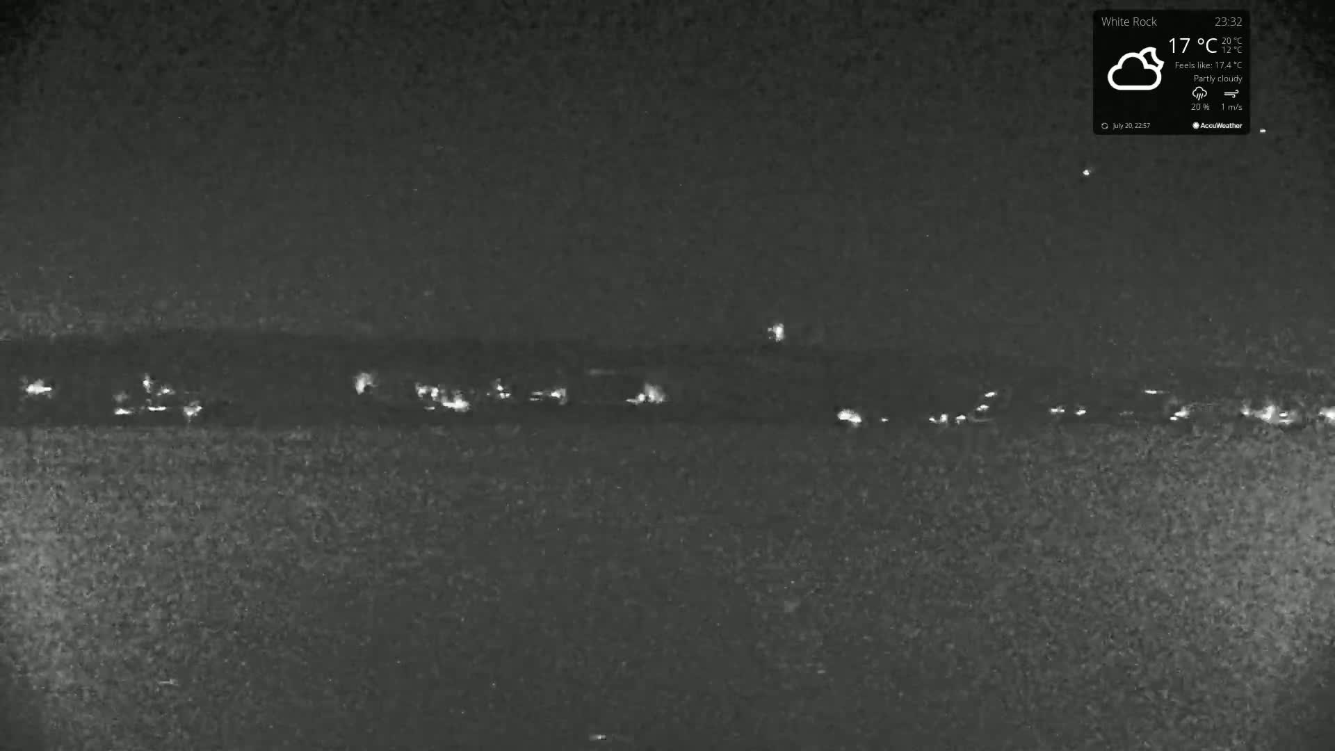 A nighttime, partly cloudy scene shows a line of distant lights possibly from vehicles or buildings.