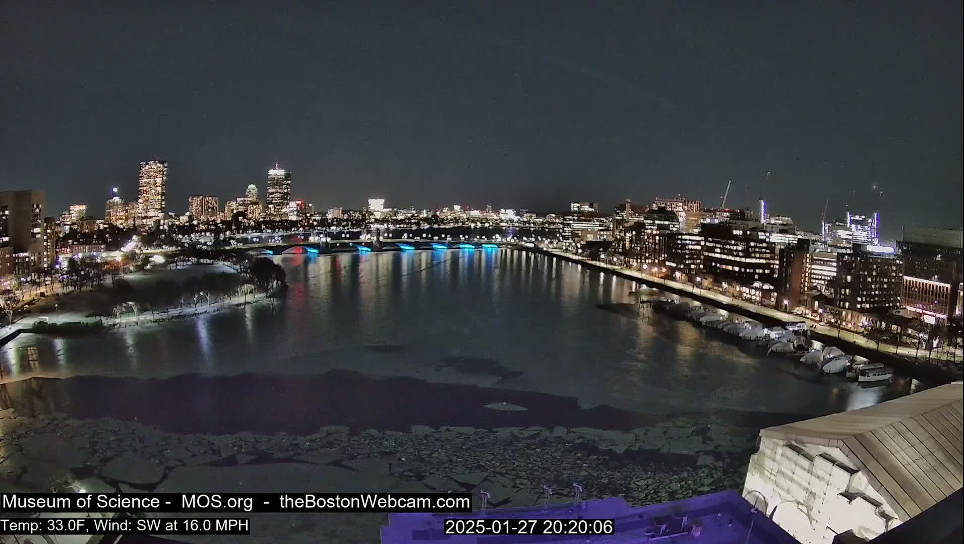 A nighttime cityscape with a partially ice-covered river, illuminated buildings, and a southwest wind at 16 mph.