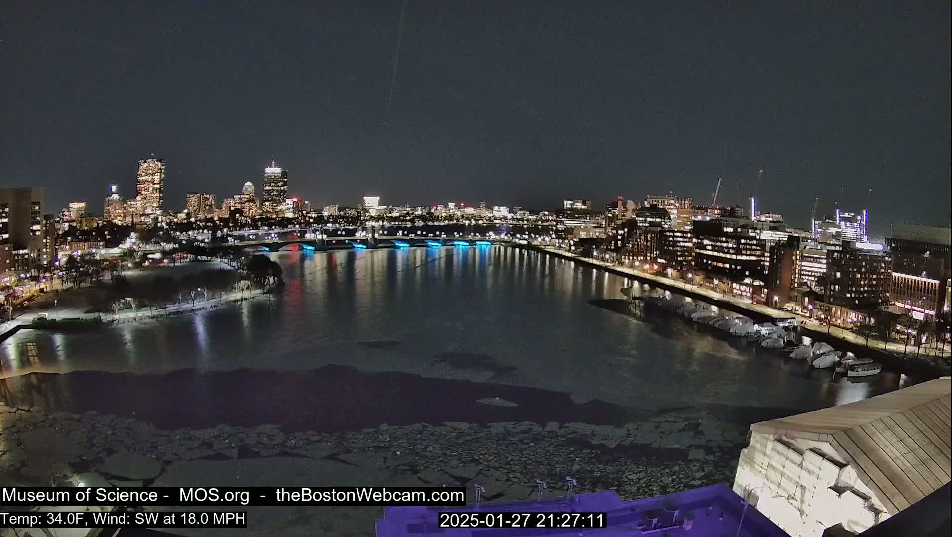 A nighttime cityscape with a partially frozen river, under a clear sky and with a southwest wind at 18 mph.