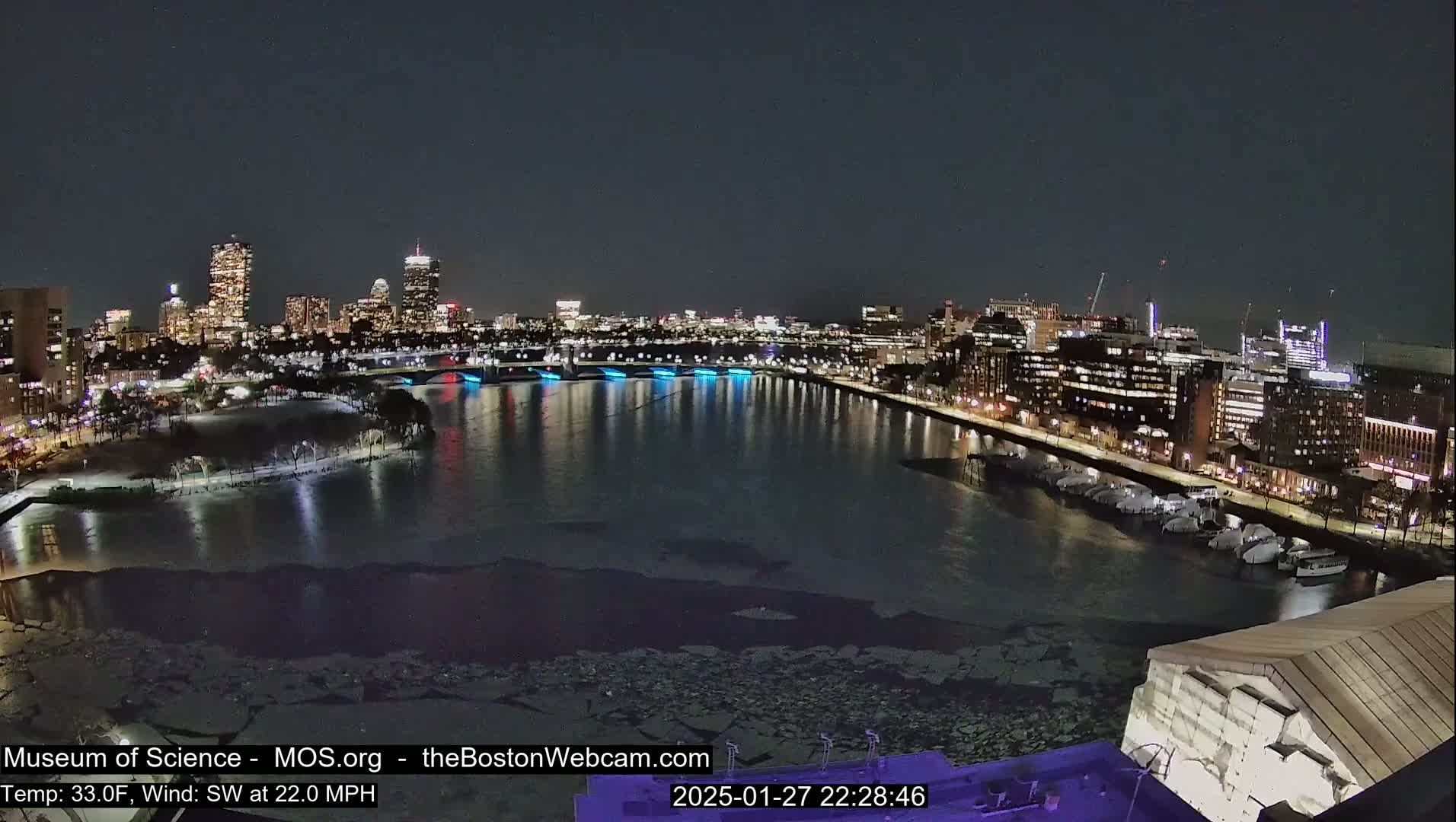 A nighttime view of a city skyline across a partially frozen river, with a southwest wind at 22 mph and a temperature of 33°F.