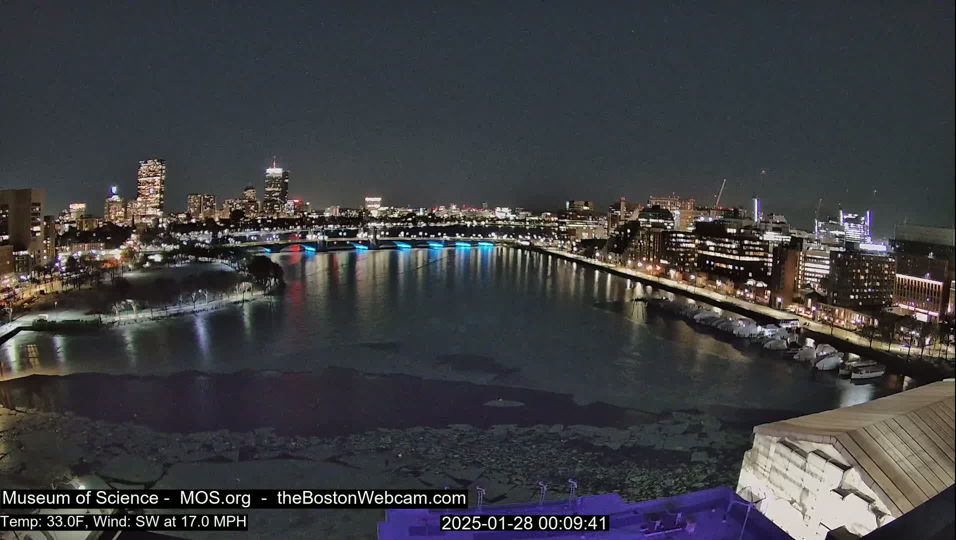 A nighttime cityscape with a river partially frozen over, illuminated buildings, and a strong southwest wind.