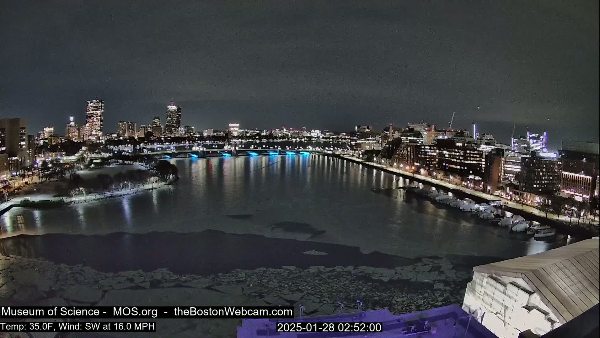 A nighttime view of a city skyline across a partially ice-covered river, with a southwest wind at 16 mph and a temperature of 35°F.