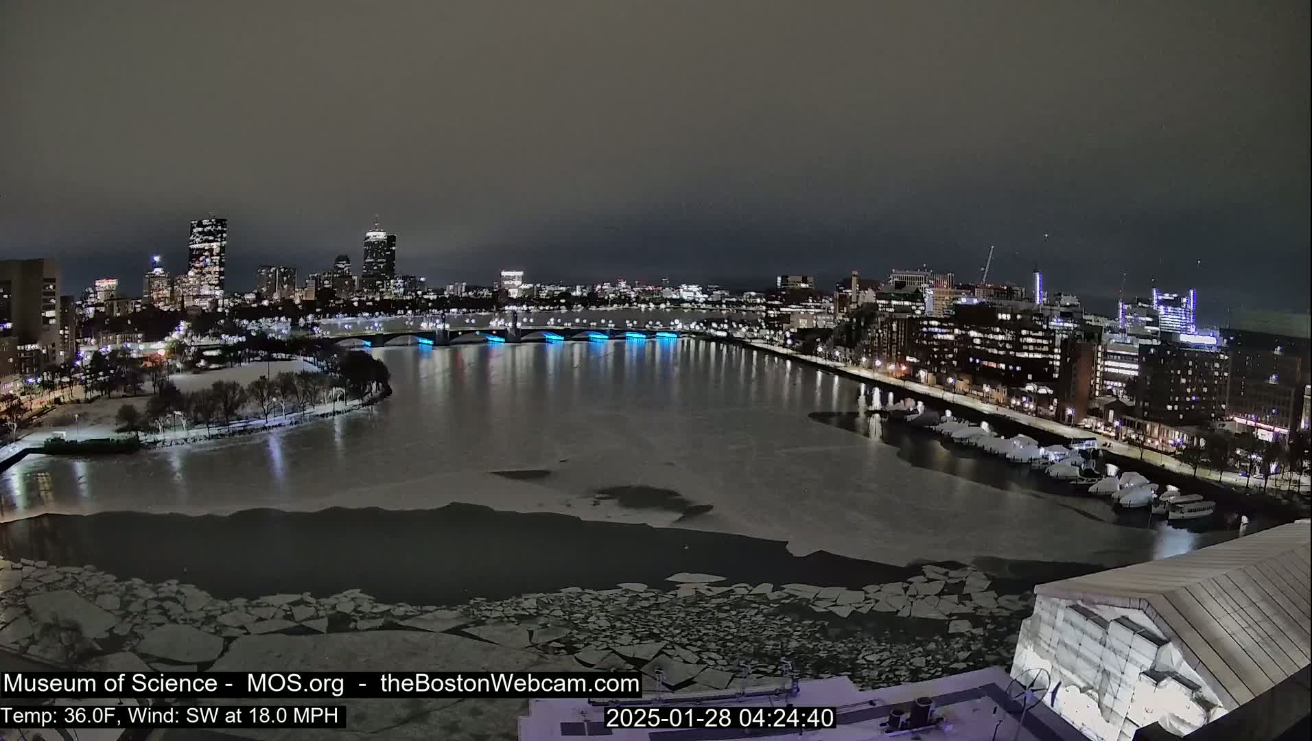 A nighttime cityscape with a partially frozen river, illuminated bridges, and a city skyline under a dark, overcast sky.