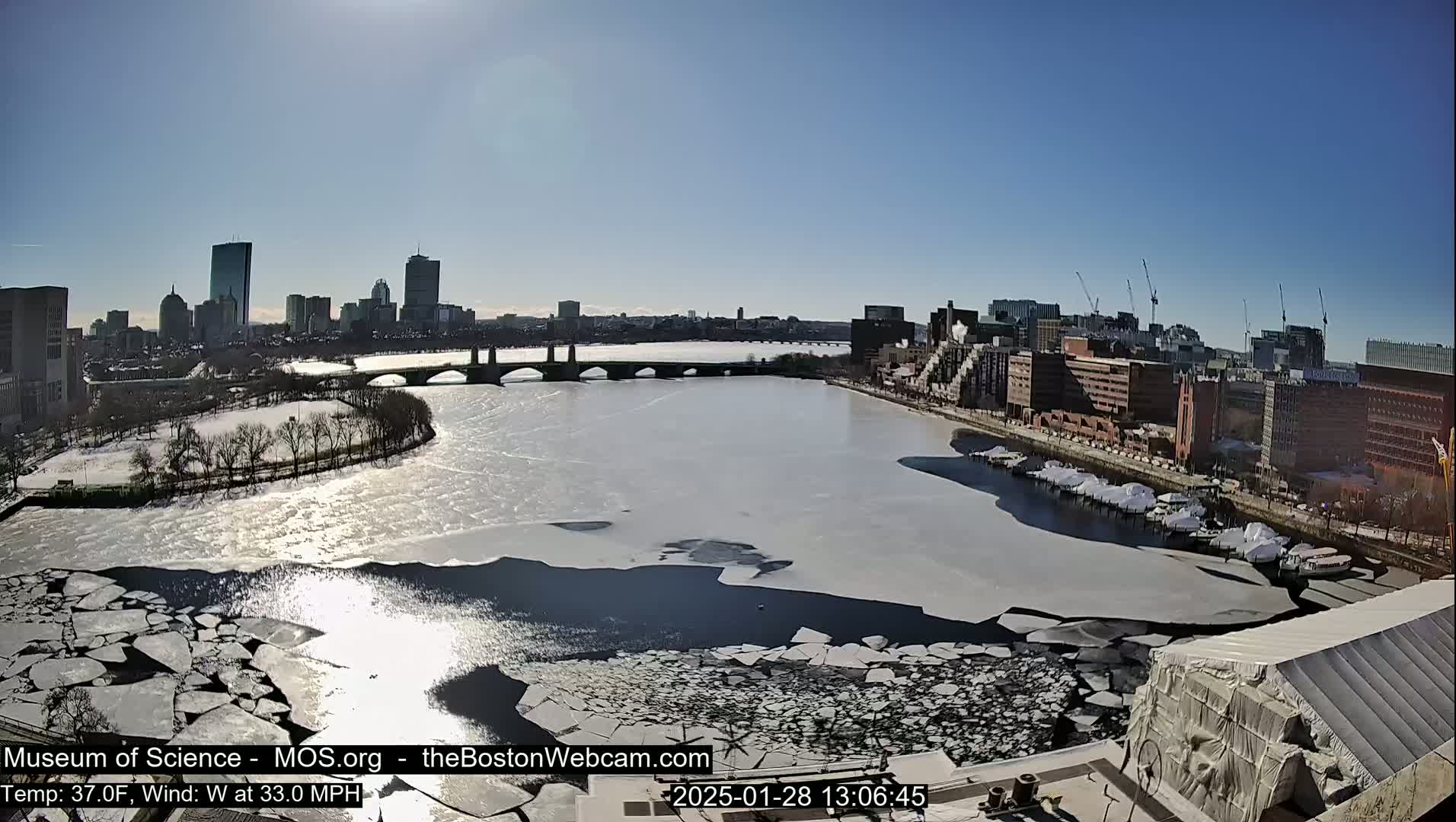 A partially frozen river flows through a city under a clear, sunny sky.