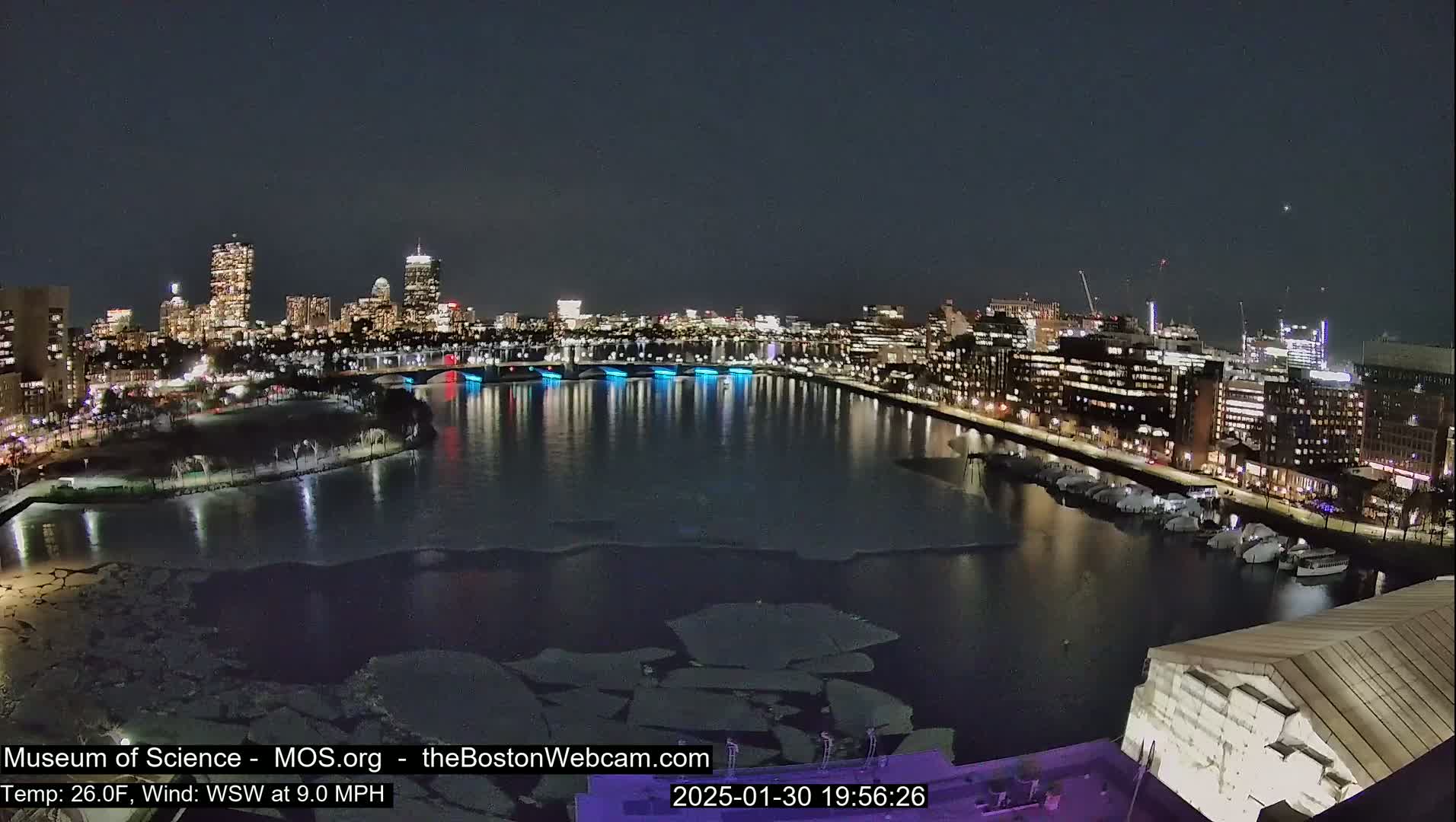 A nighttime view of a city skyline across a partially ice-covered river, under a clear sky.