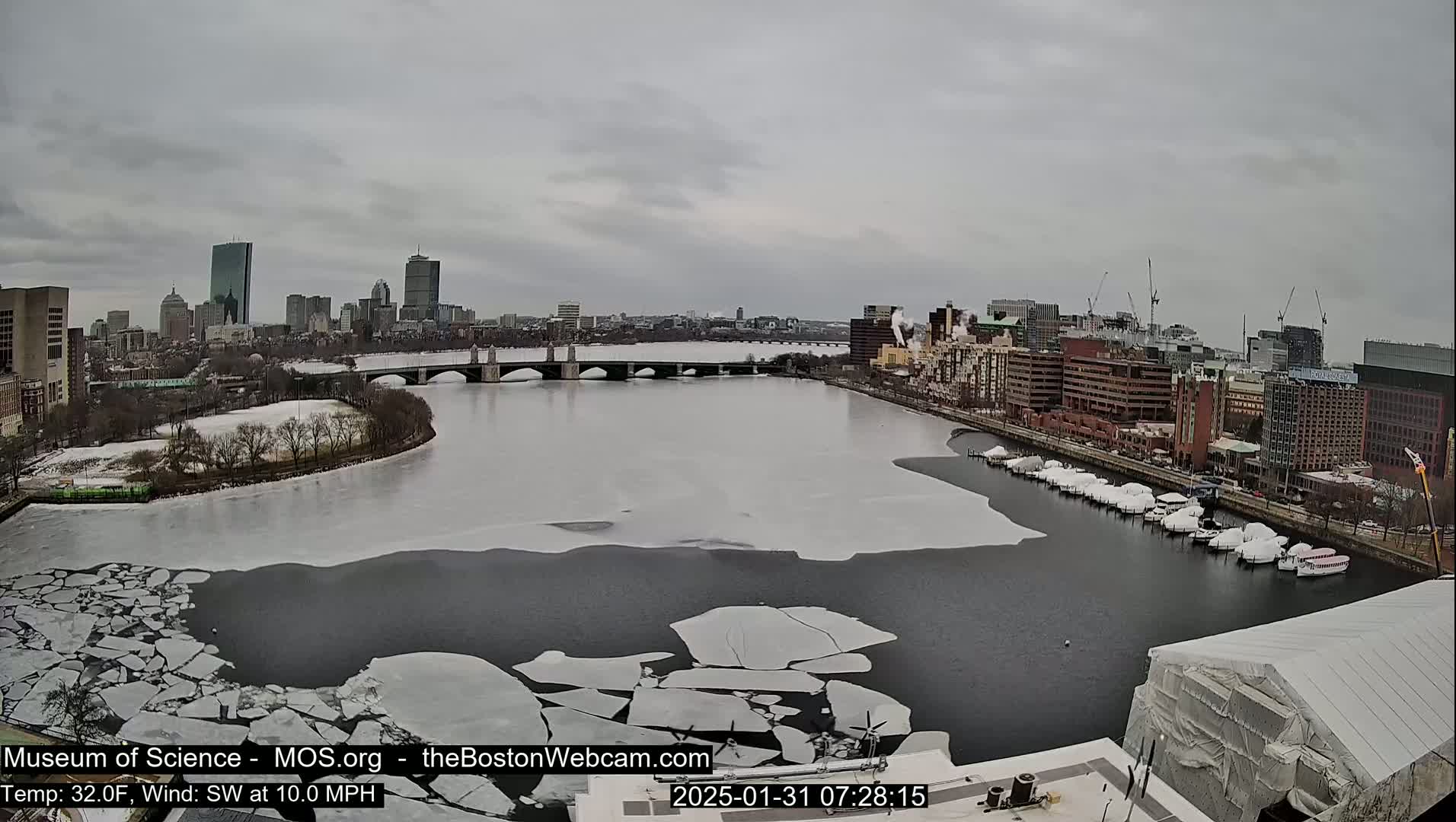 A city skyline is visible across a river partially covered in ice floes under an overcast sky.