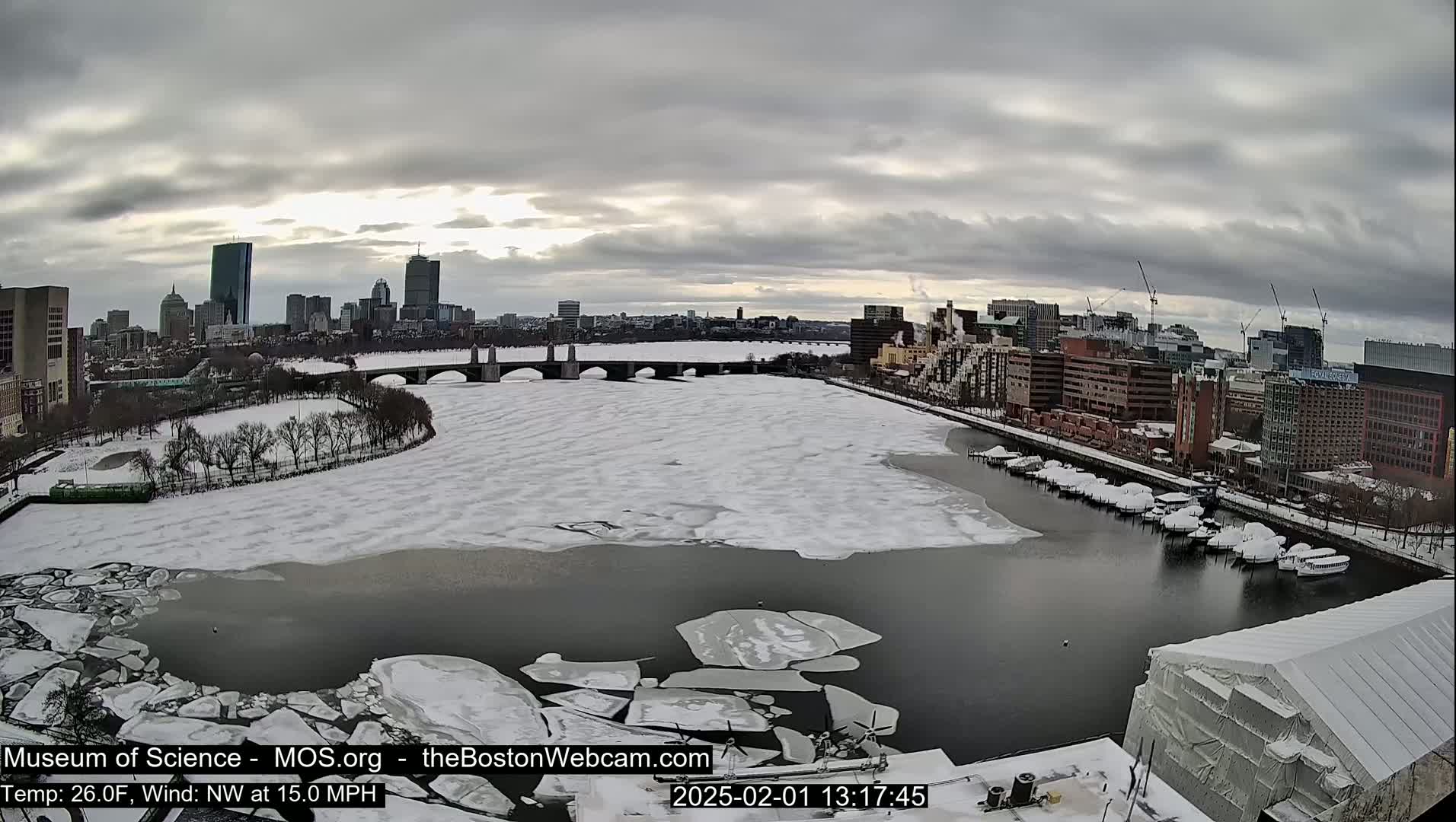 A snow-covered city and partially frozen river are seen under a cloudy sky.