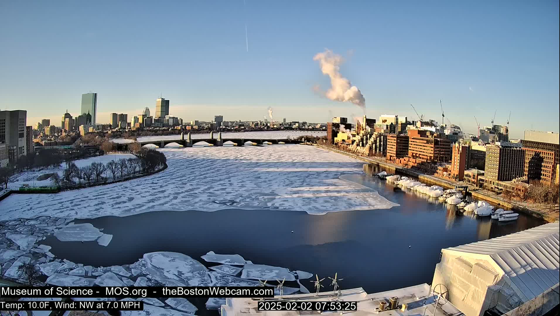 A partially frozen river flows past a city skyline on a clear, cold day.