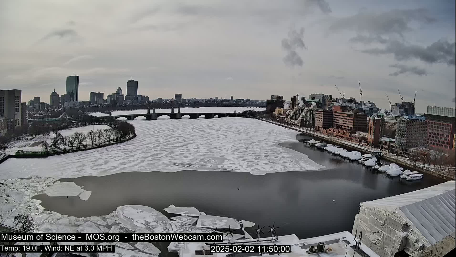 A partially frozen river flows past a city skyline under a cloudy sky.