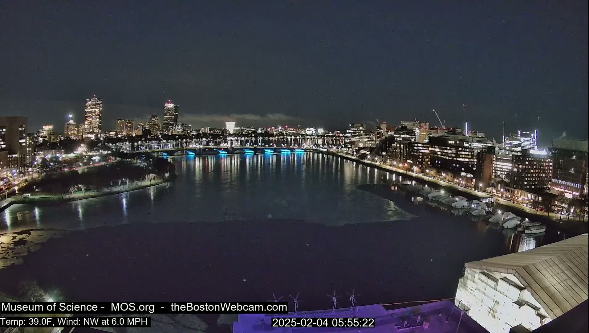 A nighttime cityscape with a river partially frozen, illuminated by city lights, under a mostly clear sky.