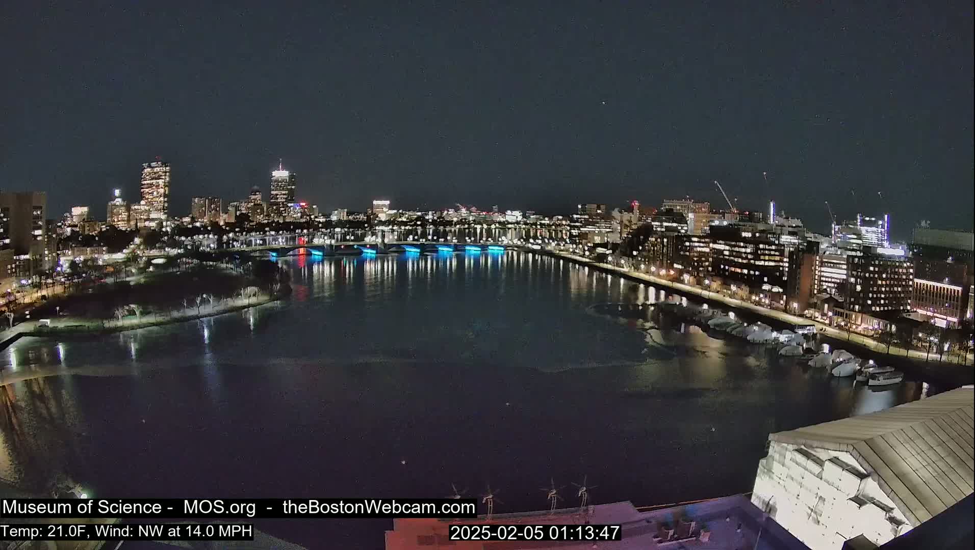 A nighttime cityscape with a river partially frozen, illuminated buildings, and a bridge with blue lights.