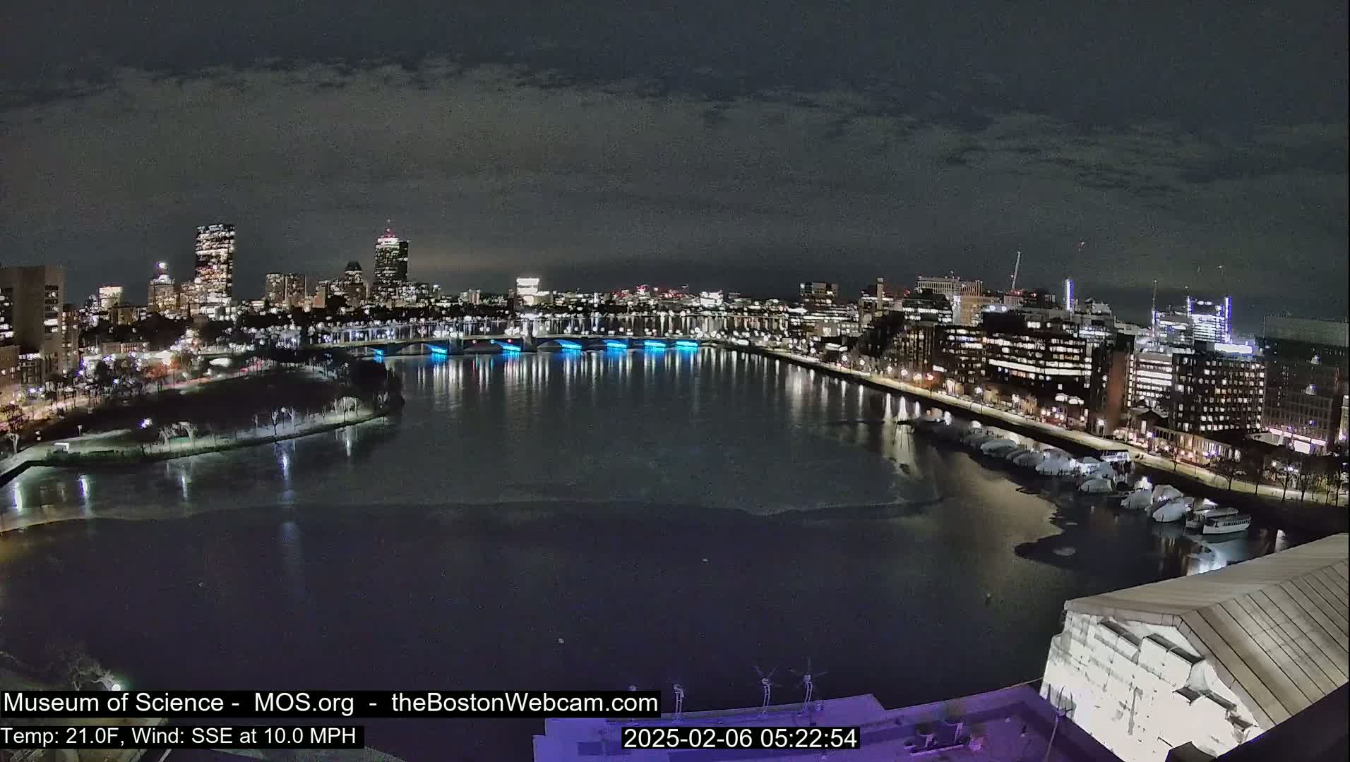 A nighttime cityscape with a partially frozen river, illuminated bridges, and city lights under a dark, cloudy sky.