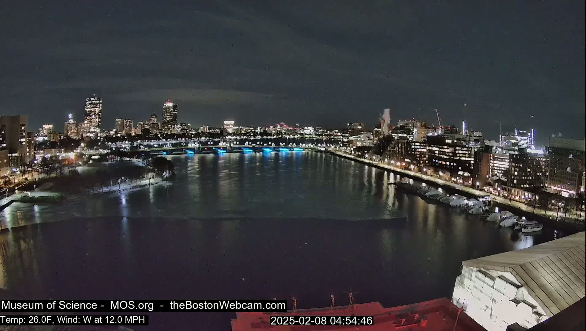 A nighttime cityscape with a partially frozen river reflecting city lights under a dark sky.