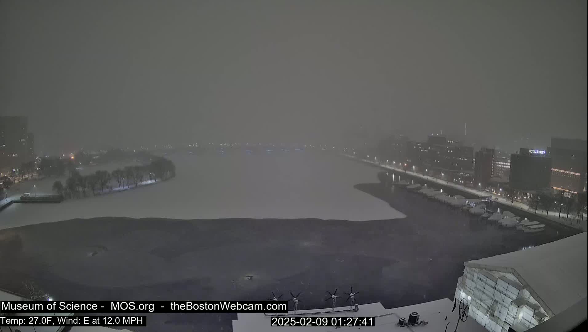 A snowstorm blankets a city waterfront at night, obscuring buildings and a partially frozen body of water.