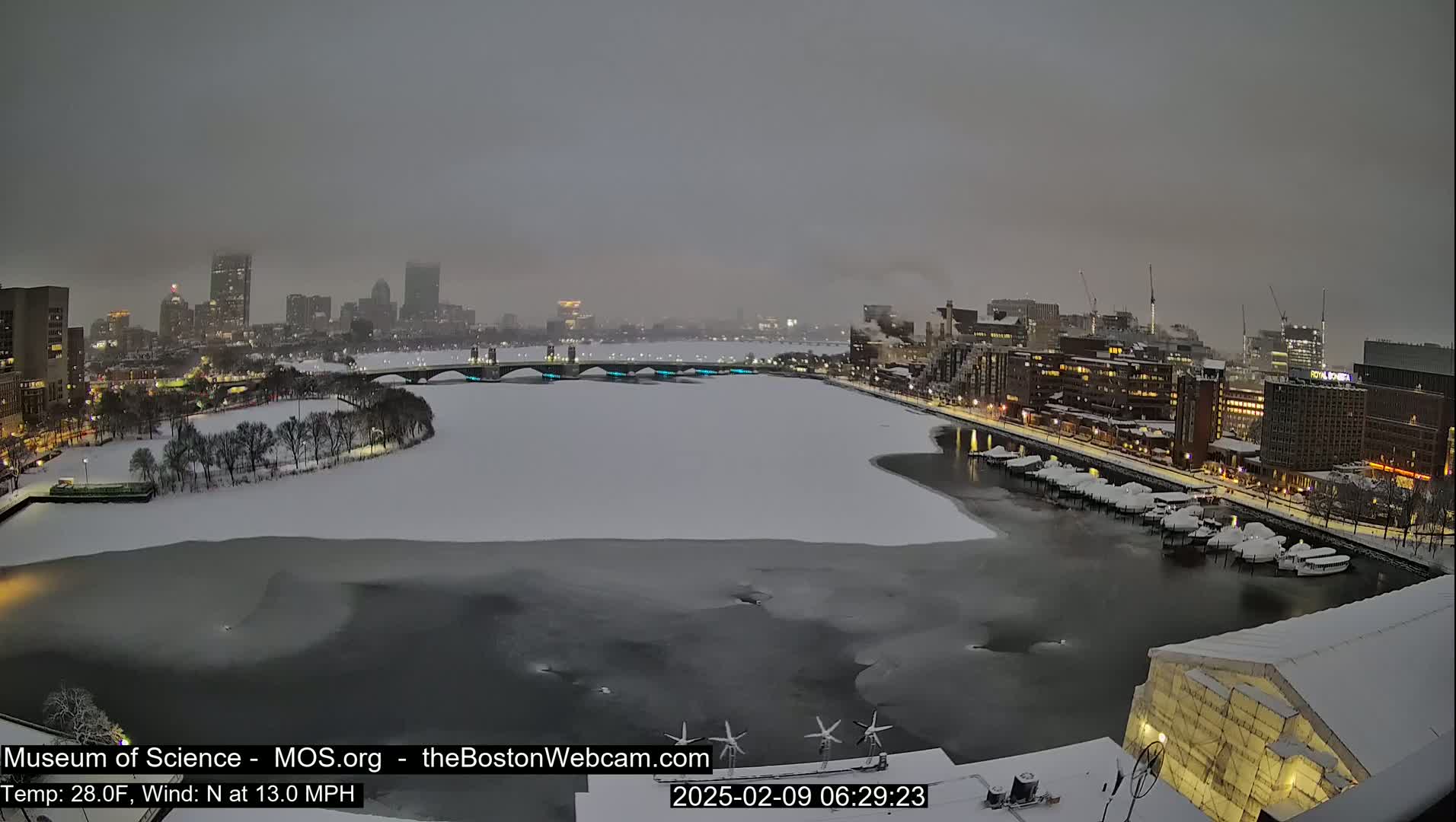 A snow-covered city skyline and partially frozen river are visible under an overcast sky.