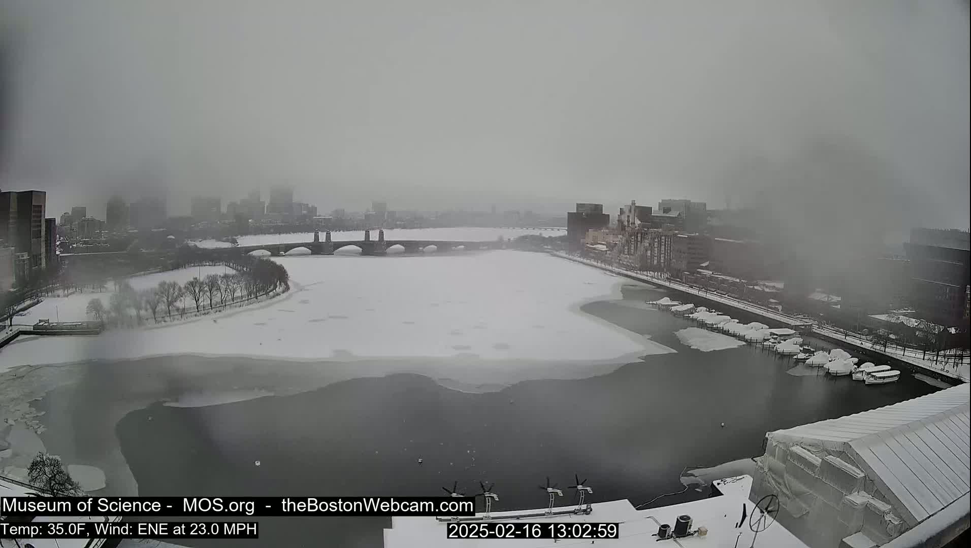 A snow-covered river and bridge are seen in a hazy, snowy cityscape.