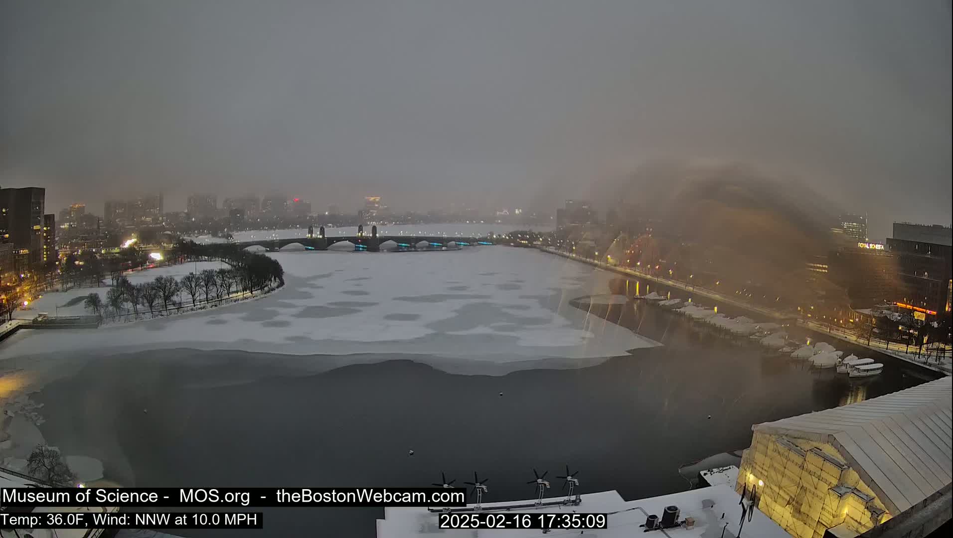 A snow-covered city landscape with a partially frozen river, under a hazy, overcast sky.