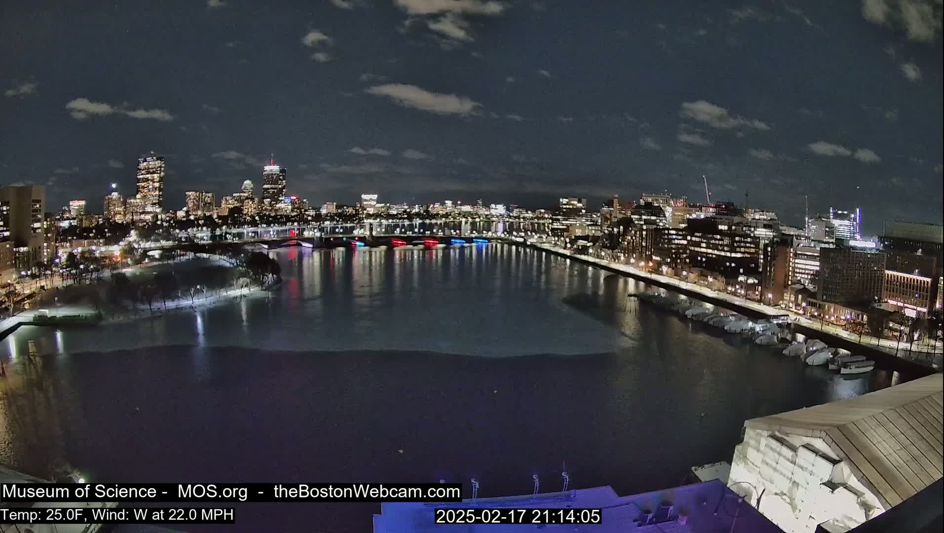 A nighttime cityscape with a partially frozen river, illuminated buildings, and a cloudy sky.