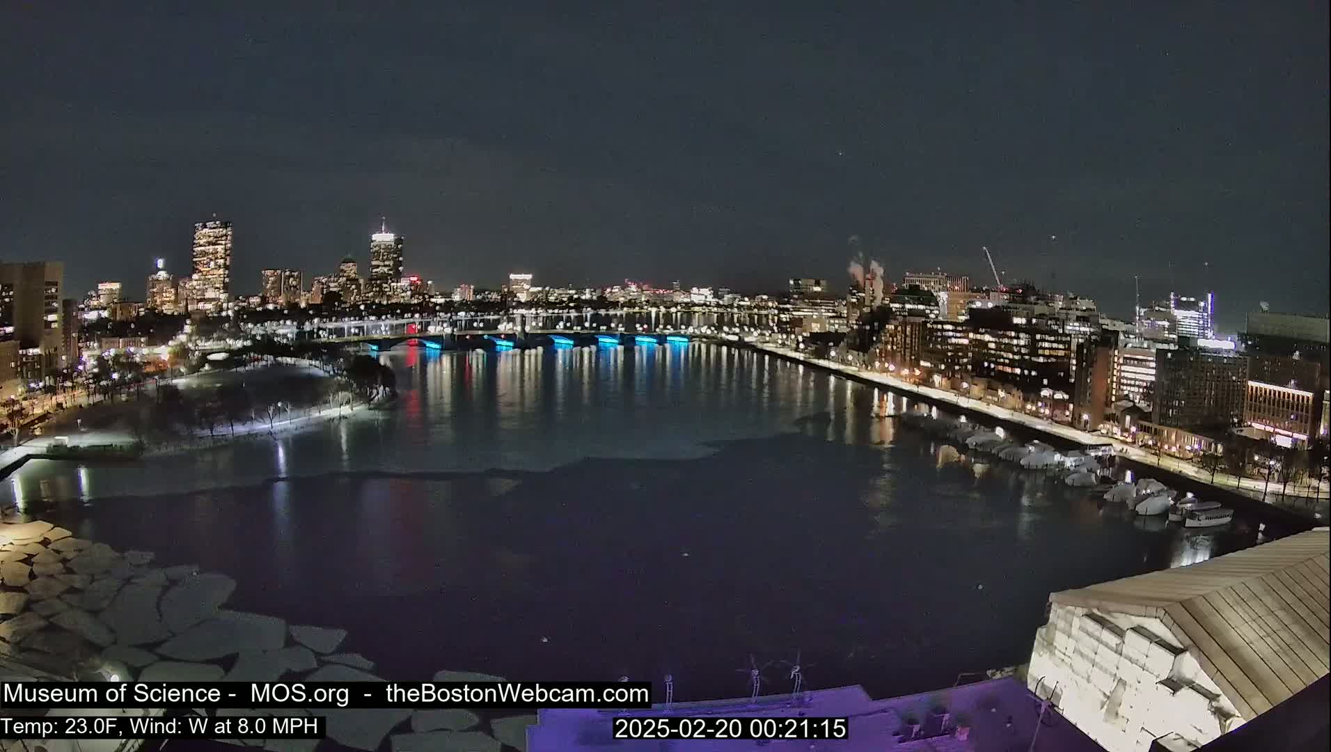 A nighttime cityscape with a partially frozen river, illuminated by city lights, under a clear, dark sky.