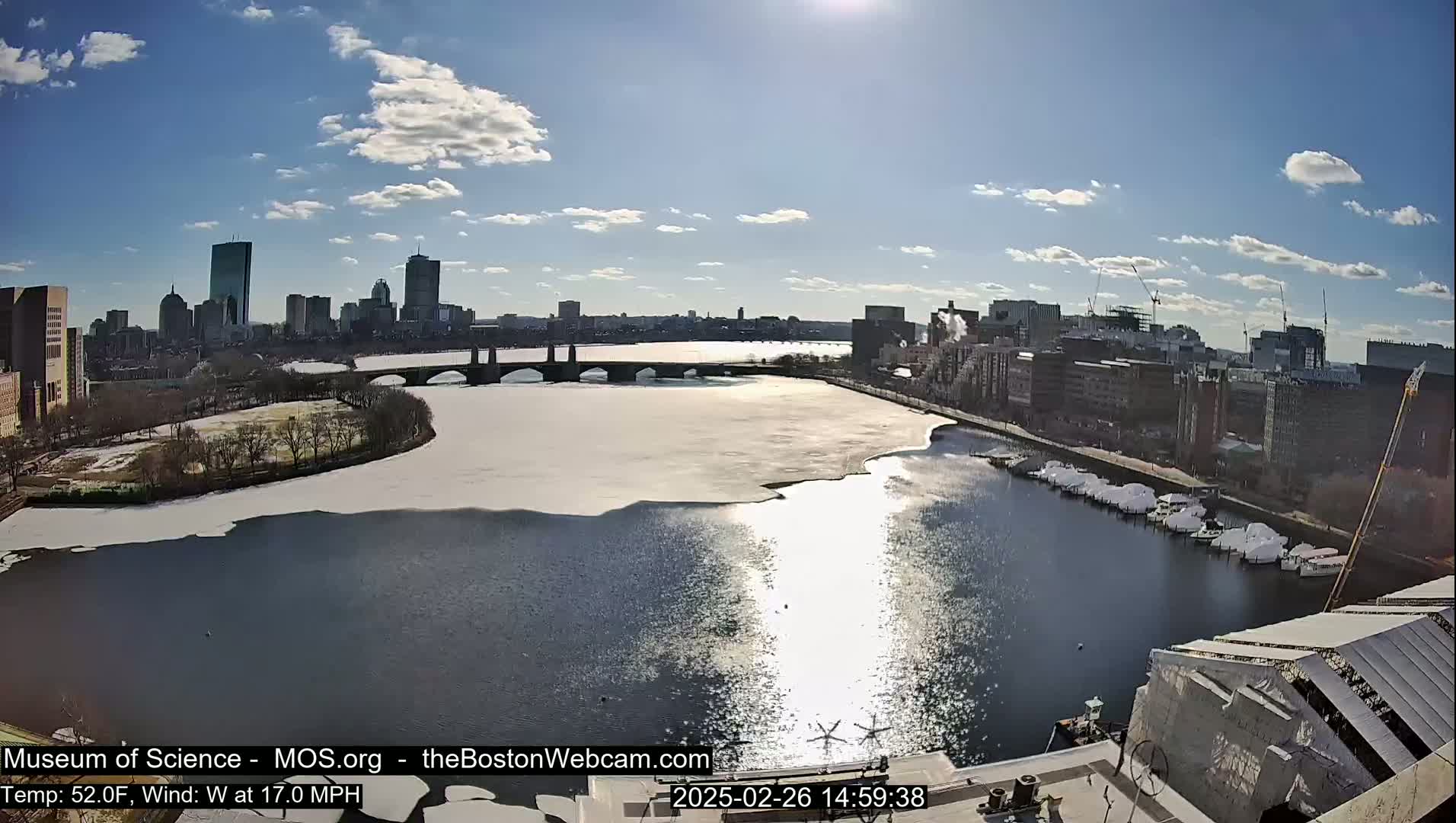 A sunny day with a 17 mph west wind shows a partially frozen river with a bridge and city skyline in the background.