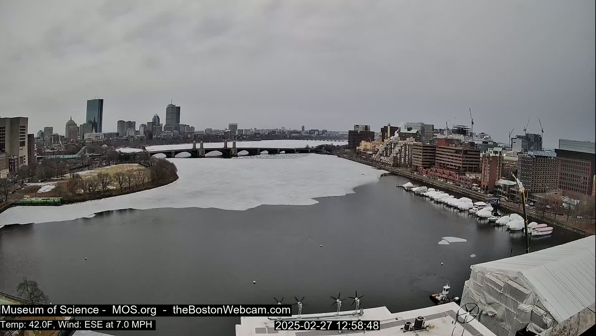 A partly icy river flows past a city skyline under an overcast sky.