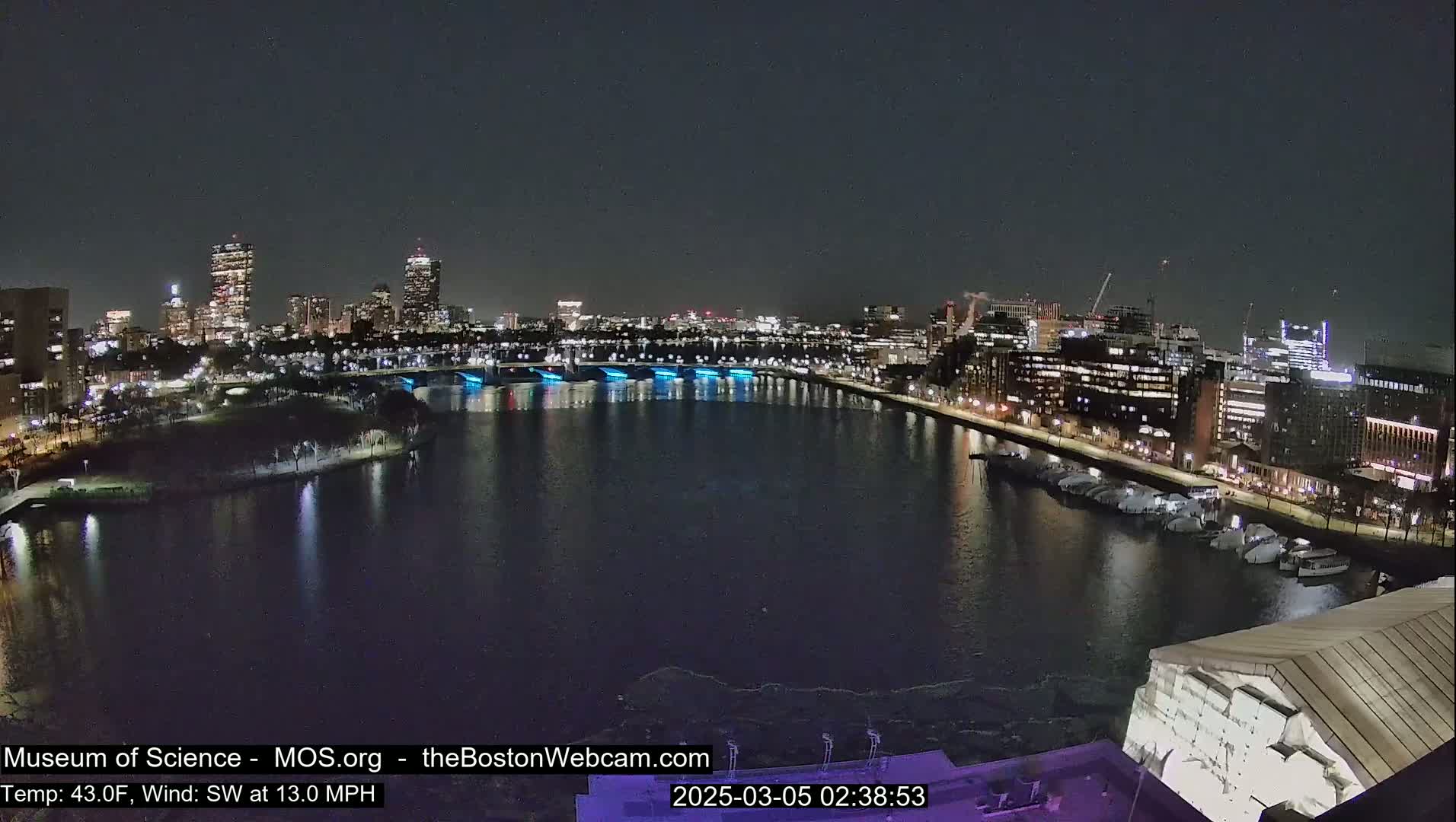 A nighttime cityscape with a river reflecting city lights, under a clear, dark sky.