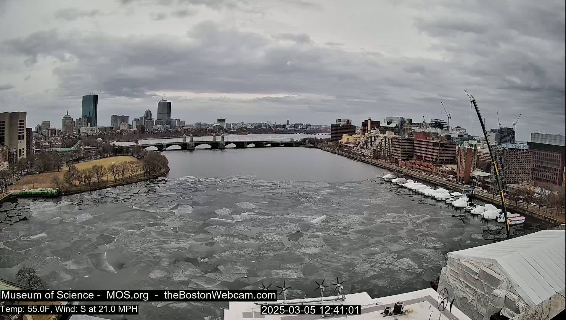 A city skyline with a river partially covered in ice flows under an overcast sky.