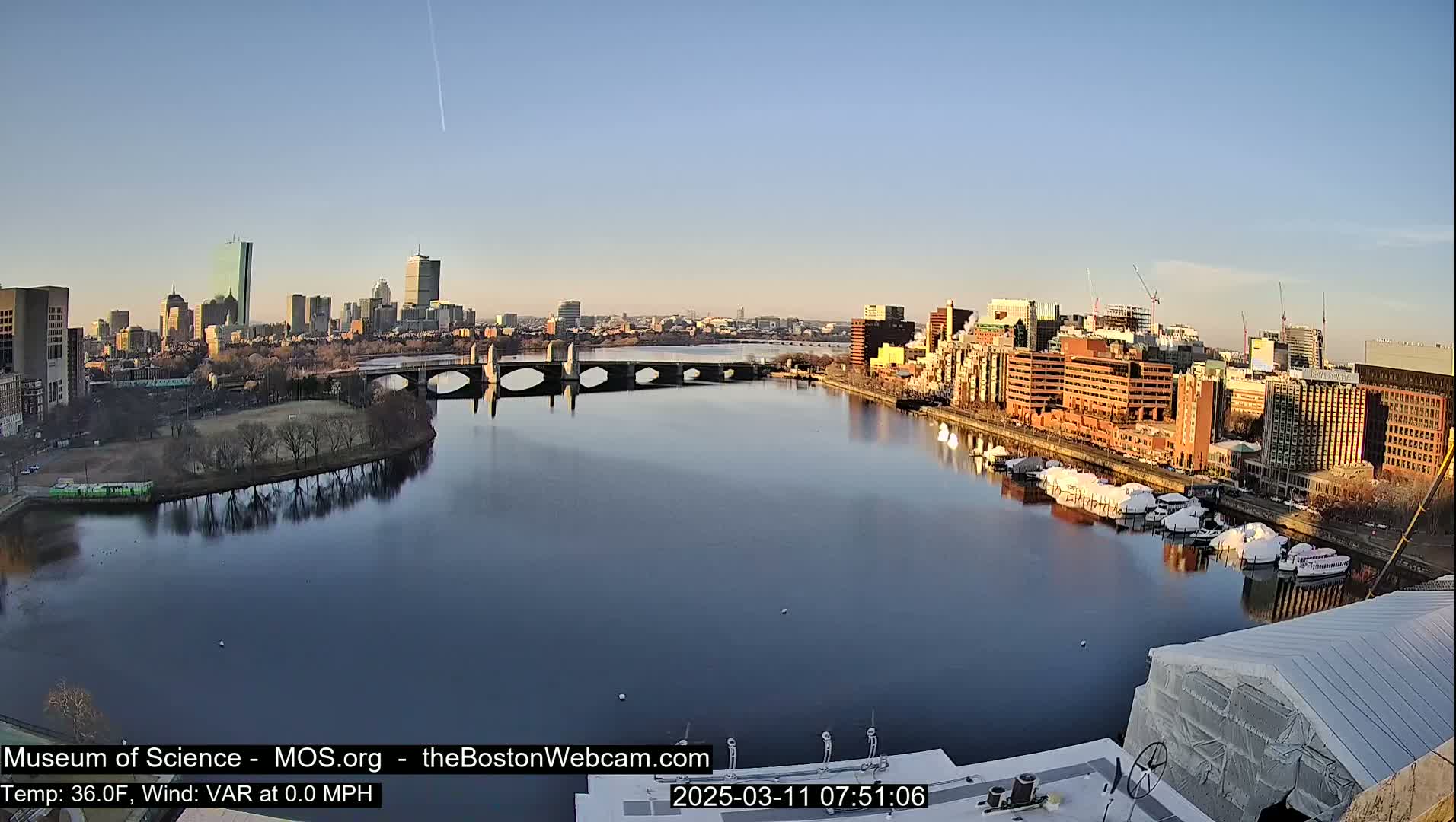 A calm river reflects a cityscape under a clear, bright sky.