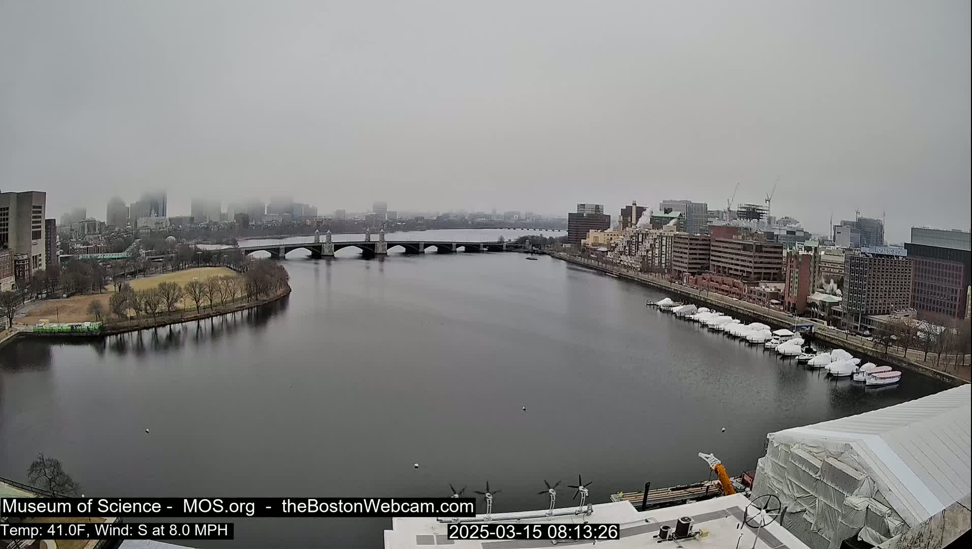 A foggy cityscape with a river, bridge, and docked boats is visible from a high vantage point.