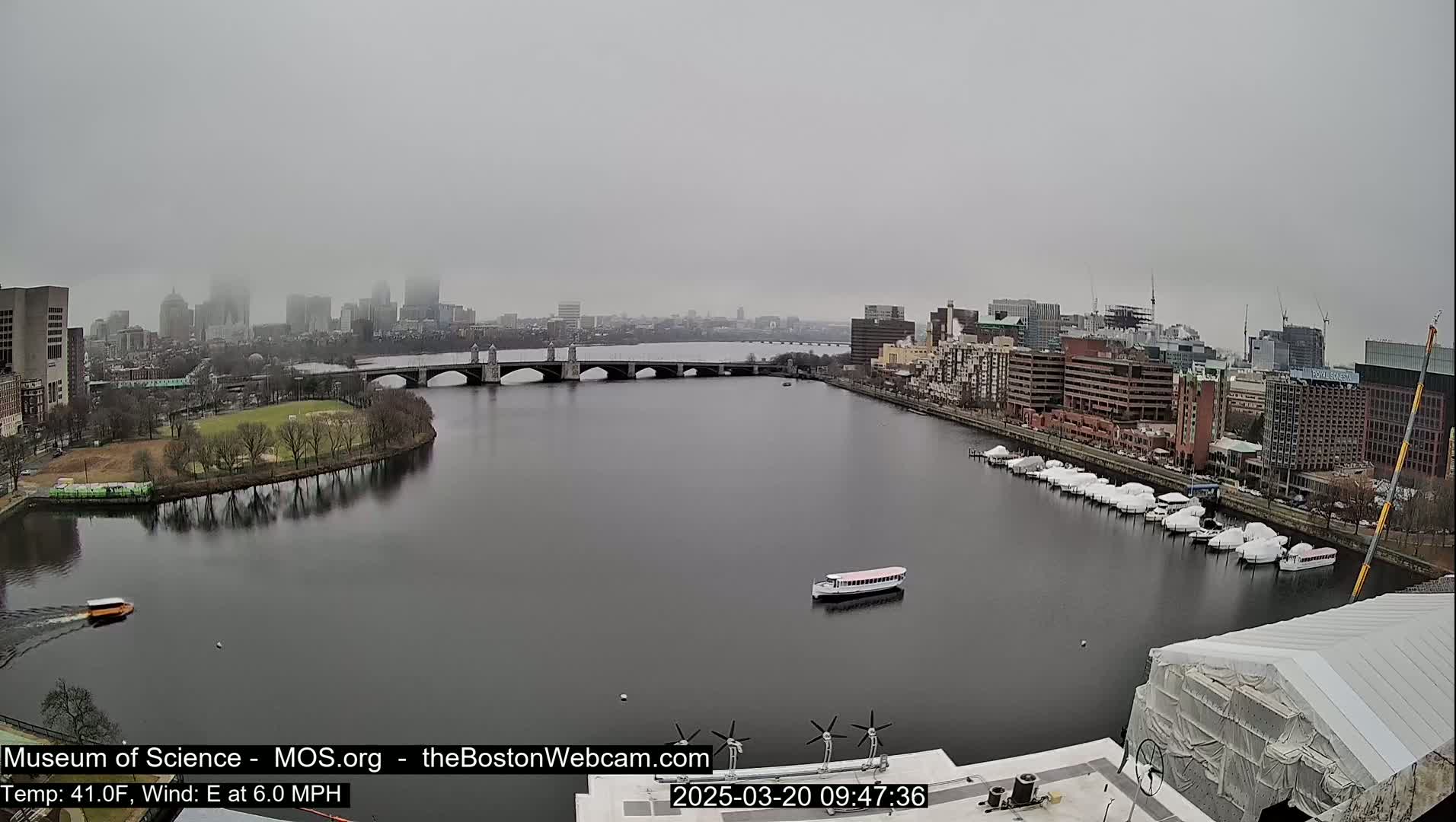 A foggy cityscape with a river, bridge, and docked boats is visible from a high vantage point.