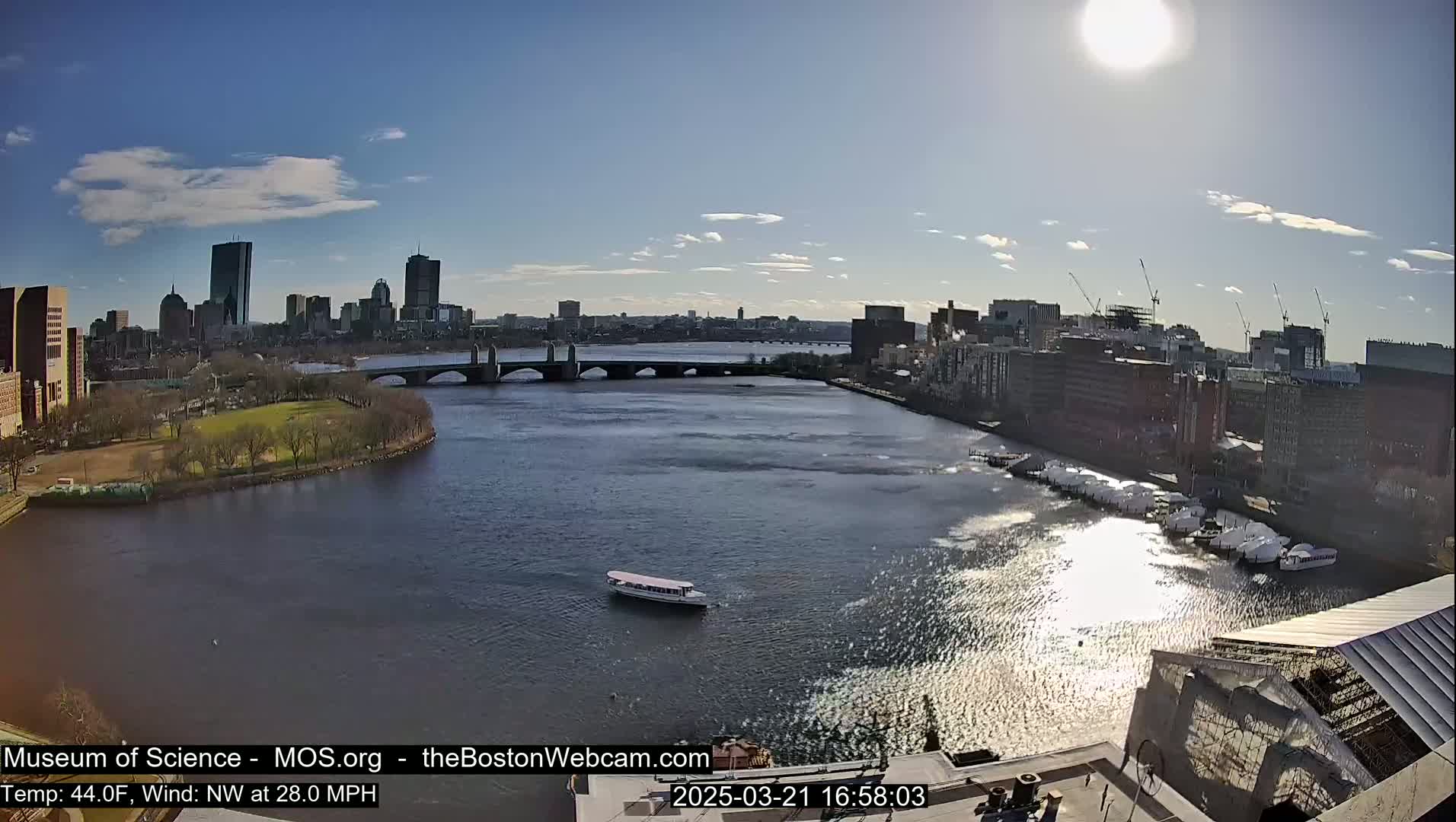 A sunny day with a northwest wind reveals a city skyline across a river, featuring a bridge and boats moored along the shore.
