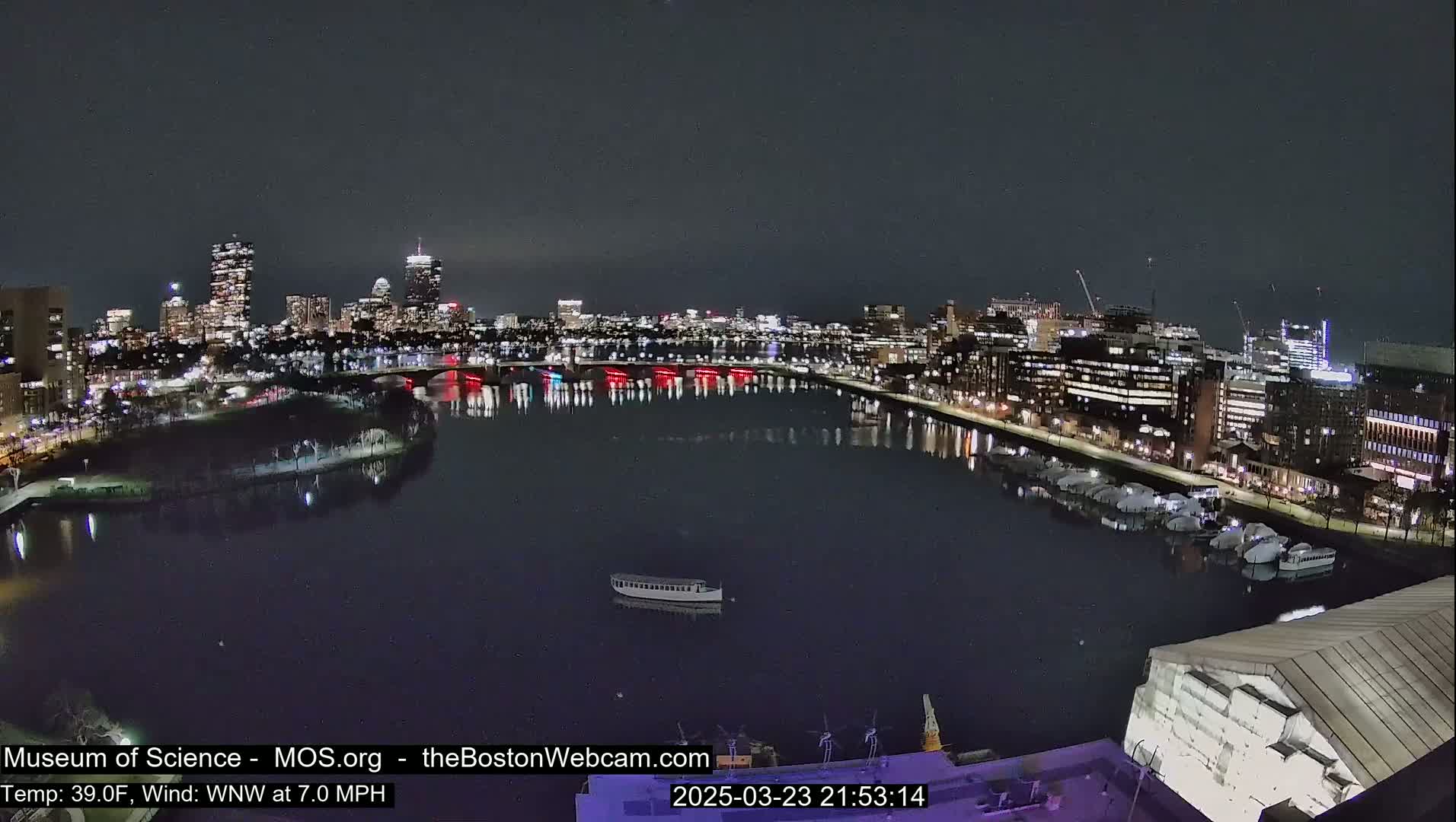 A nighttime cityscape with a calm river reflecting city lights, under a clear dark sky.