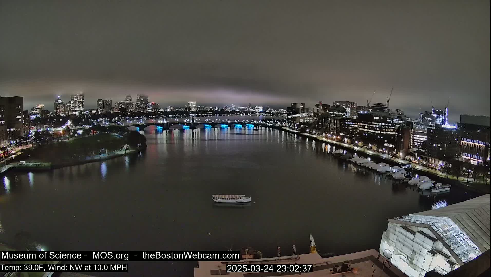 A nighttime view of a city skyline across a calm river, under a cloudy sky.