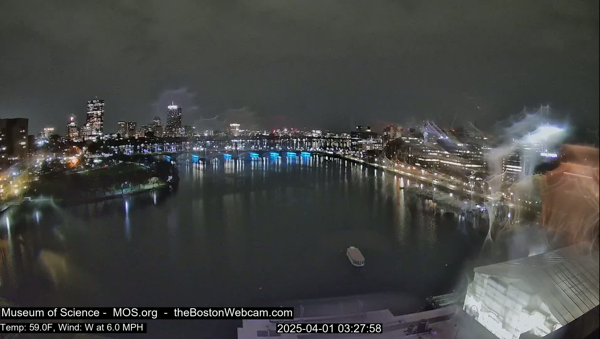 A nighttime cityscape with a body of water reflecting city lights under a dark, cloudy sky.