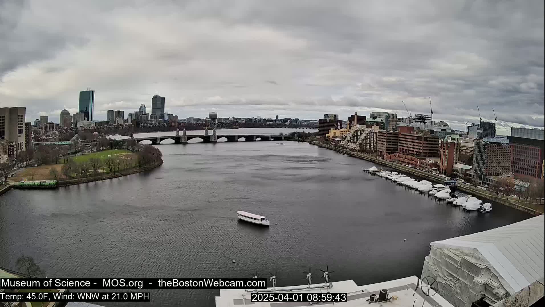 A river with a bridge and a city skyline in the background under an overcast sky.