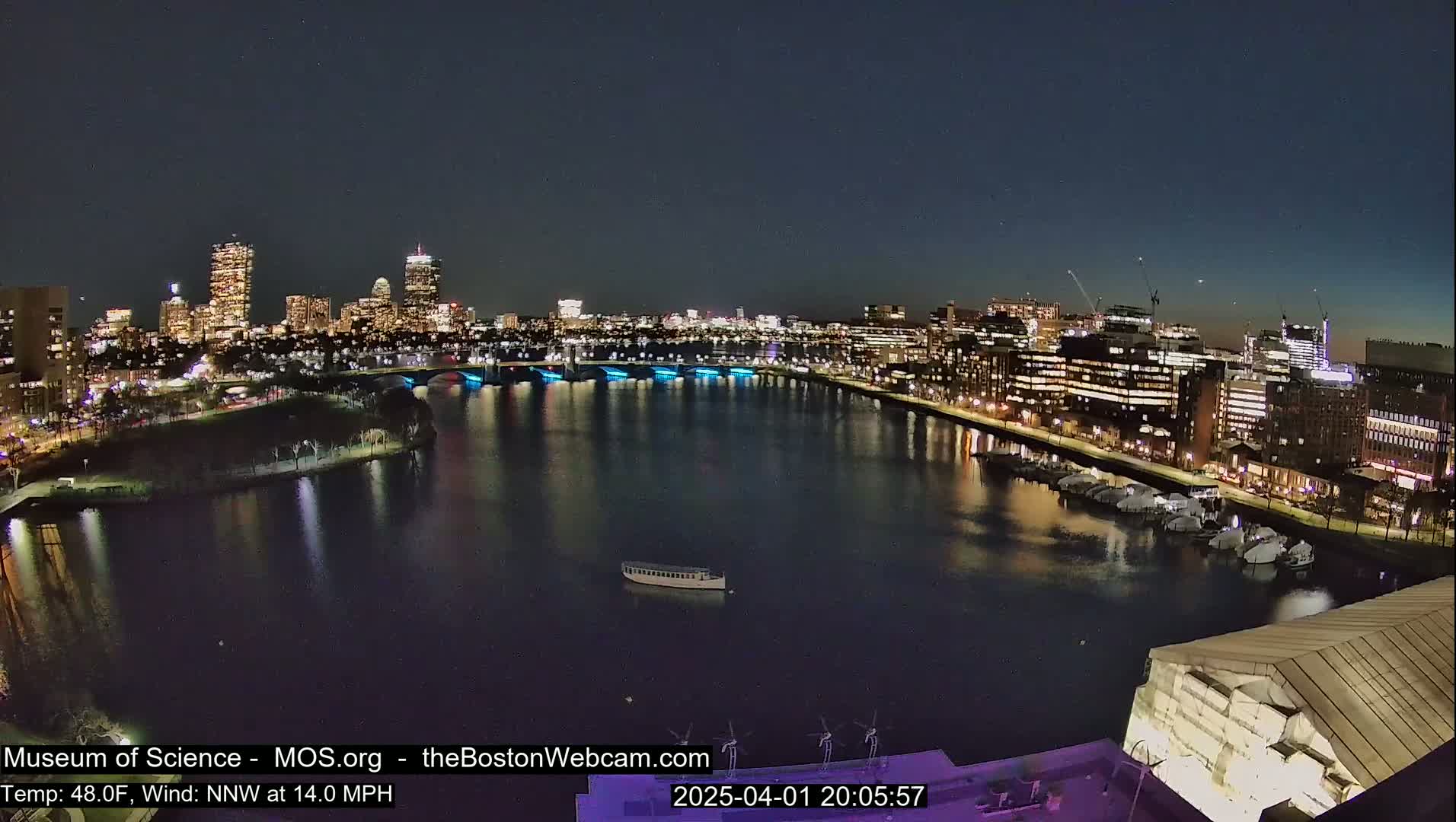 A nighttime view of a city skyline across a calm body of water, illuminated by city lights, under a clear, dark sky.