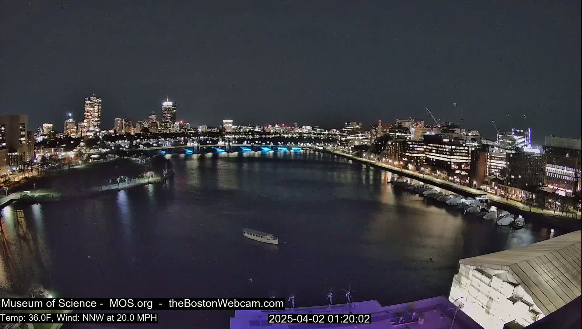 A nighttime view of a city skyline across a dark river, with a strong northwest wind.