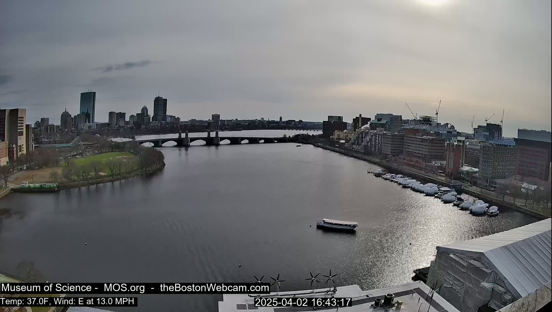 A city skyline with a bridge over a river, under a partly sunny, overcast sky.