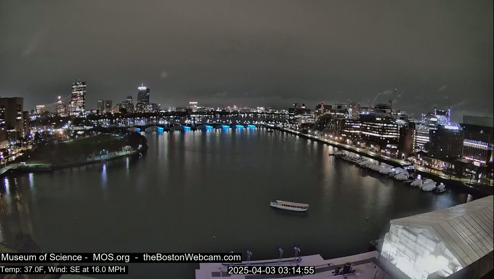 A nighttime cityscape with a body of water, illuminated bridges, and a boat, under a dark, overcast sky.