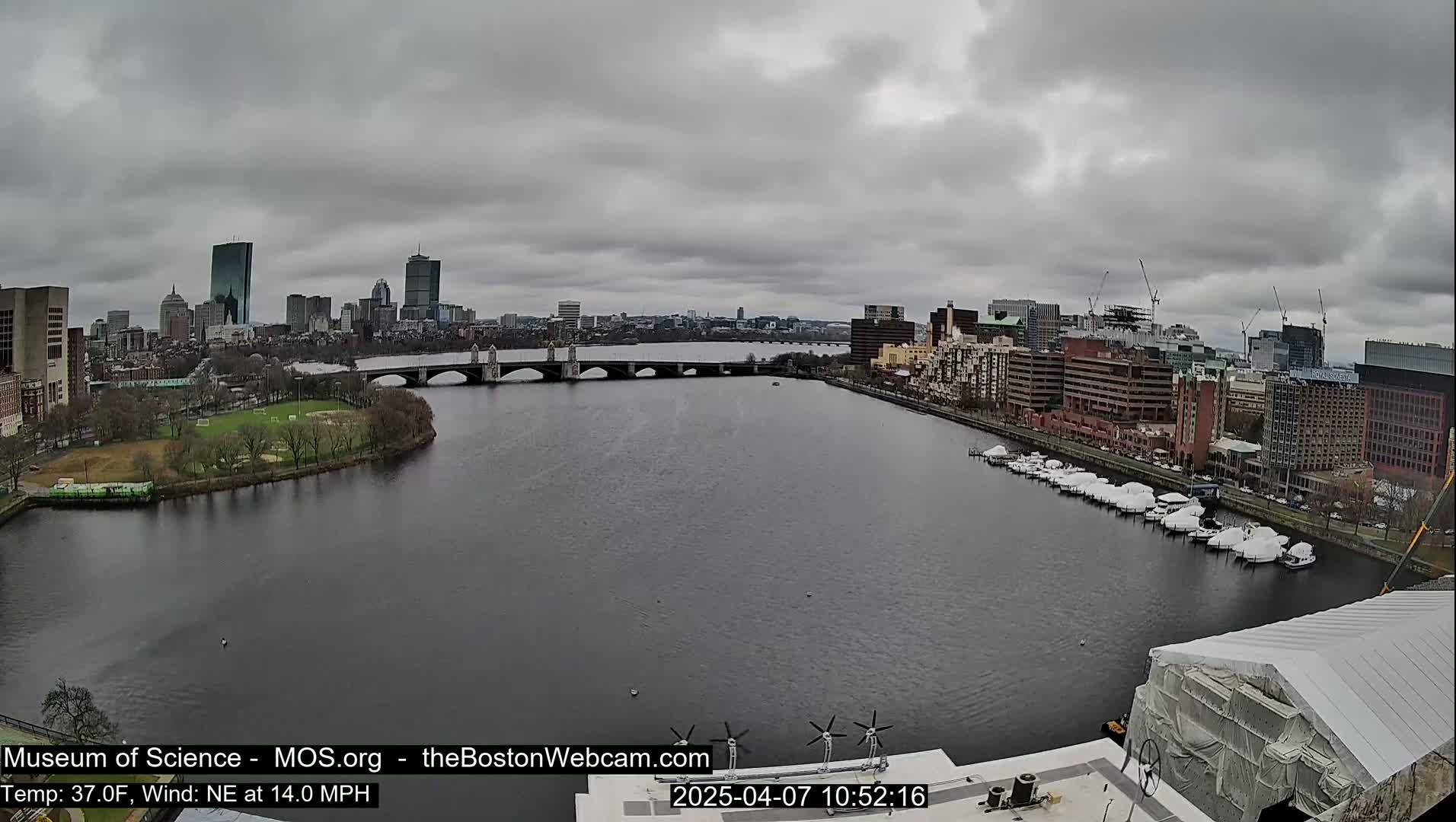 A wide shot of a river with a bridge and cityscape in the background under an overcast sky.